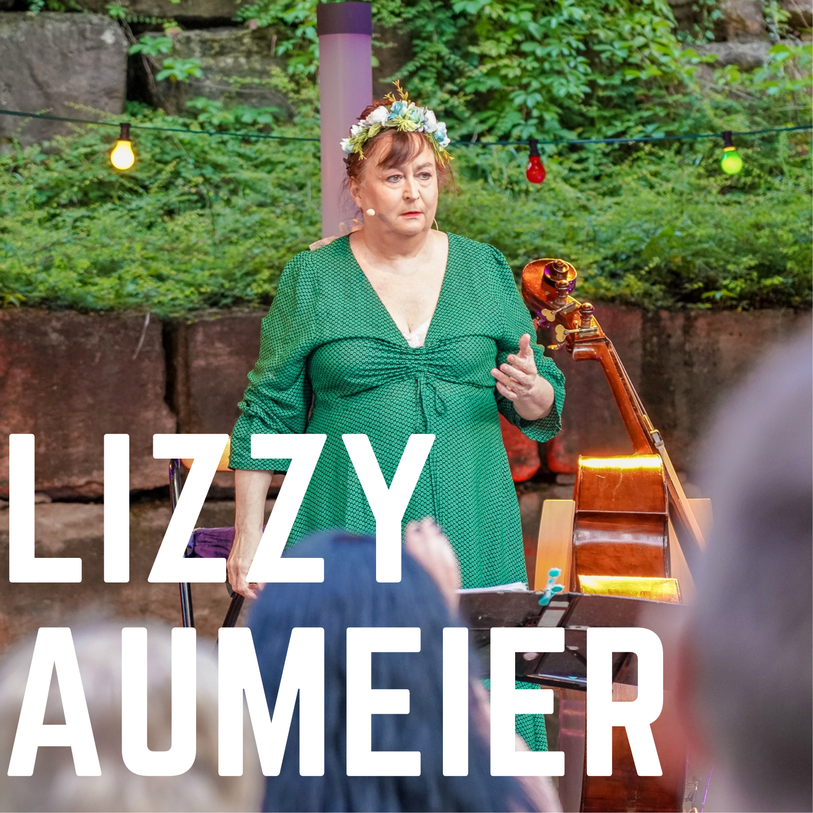 Bild vergrößern: Der Name der Künstlerin "Lizzy Auermeier" ist in weißen Blockbuchstaben auf dem Foto zu sehen. Im Hintergrund ist die Kabarettistin Lizyy Aumeier auf der Open-Air Bühne des Kultursommer 2021 zu sehen.