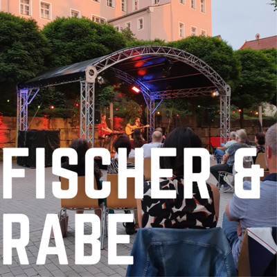 Bild vergrößern: Die Aufschrift "Fischer & Rabe" in weißen Druckbuchstaben ist auf dem Foto abgebildet. Im Hintergrund ist die Musikgruppe Fischer und Rabe auf der Open-Air Bühne des Kultursommer 2021 zu sehen.