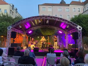 Bild vergr&ouml;&szlig;ern: Das Publikum lauscht der Italo-Pop S�ngerin Luca Vasta und ihrer Band beim Schwandorfer Kultursommer im Spitalgarten. Sie spielt auf einer Akustikgitarre.