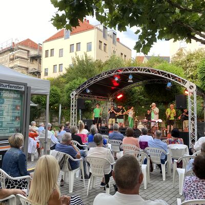 Das Publikum blickt auf die neun Musikerinnen und Musiker der Band "Skavaria" auf der Bühne des Schwandorfer Kultursommers im Spitalgarten. Alle tragen ein grünes Kleidungsstück.