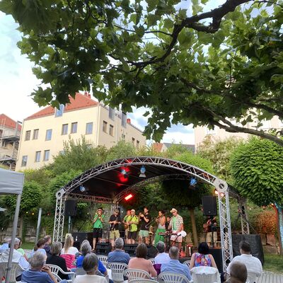 Das Publikum blickt auf die neun Musikerinnen und Musiker der Band "Skavaria" auf der Bühne des Schwandorfer Kultursommers im Spitalgarten. Alle tragen ein grünes Kleidungsstück.