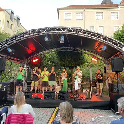 Die neun Musikerinnen und Musiker der Band "Skavaria" auf der Bühne des Schwandorfer Kultursommers im Spitalgarten. Alle tragen ein grünes Kleidungsstück.