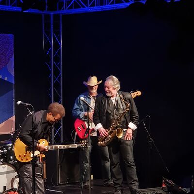 Foto von drei Musikern der al jones band mit Gitarren und Saxophon auf der Open-Air Bühne.