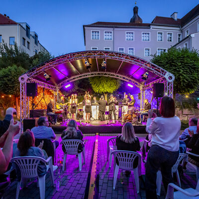 Das Publikum lauscht dem Auftritt der Band BULs Brothers beim Schwandorfer Kultursommer im Spitalgarten. Der Spitalgarten ist während der Dämmerung stimmungsvoll beleuchtet.