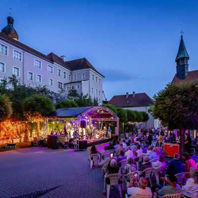 Das Publikum lauscht dem Auftritt der Band BULs Brothers beim Schwandorfer Kultursommer im Spitalgarten. Der Spitalgarten ist während der Dämmerung stimmungsvoll beleuchtet.