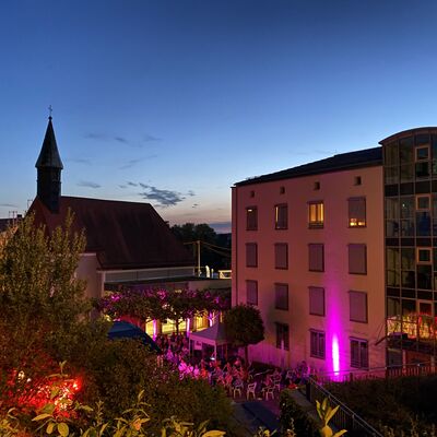 Blick von oben in den stimmungsvoll beleuchteten Spitalgarten vor dem Schwandorfer Rathaus. Im Hintergrund ist die Spitalkirche in der Dämmerung zu sehen.