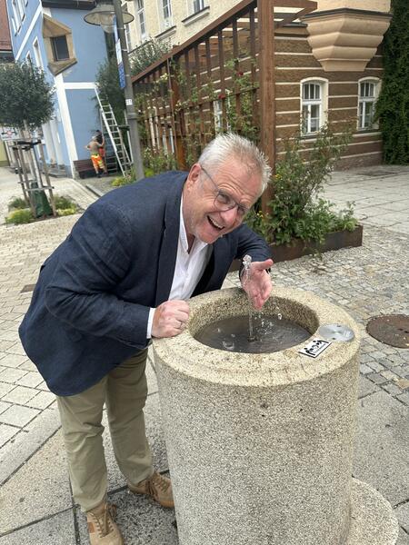 Bild vergrößern: Ein Mann erfrischt sich an einem Brunnen.