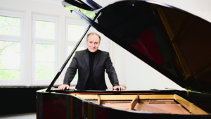 Bild vergrößern: Portrait des Pianisten Christian Seibert. Er steht hinter einem geffneten Flgel