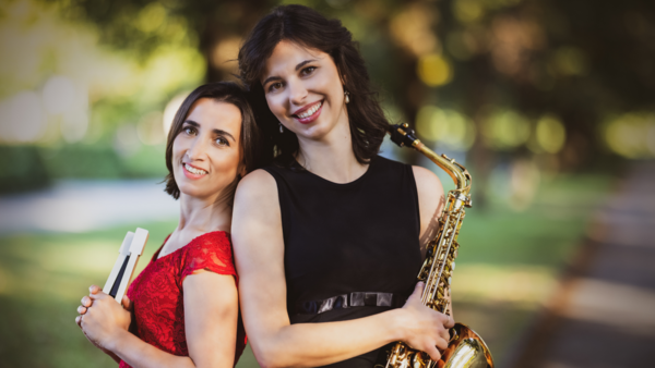 Bild vergrößern: Portrait der beiden Musikerinnen des Duo Millefleurs. Rechts die Pianistin Nestan Heberger in einem roten Kleid. Links, (Rücken an Rücken) Sarah Lilian Kober in schwarzem Kleid und mit Saxophon.