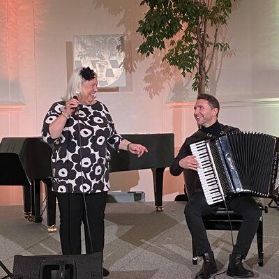 Die Sängerin Tuija Komi singt auf der Bühne der Spitalkirche in ein Mikrofon. Neben ihr sitzt der Musiker Vlad Cojocaru am Akkordeon.