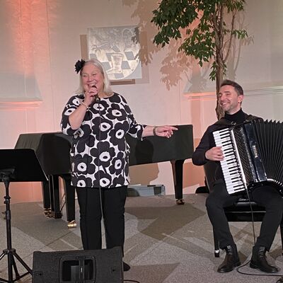 Die Sängerin Tuija Komi singt auf der Bühne der Spitalkirche in ein Mikrofon. Neben ihr sitzt der Musiker Vlad Cojocaru am Akkordeon.