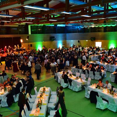 Foto in Vogelperspektive vom Stadtball in der Oberpfalzhalle. Die Halle ist grün erleuchtet. Menschen in Abendgarderobe tanzen auf der Tanzfläche oder sitzen an festlich gedeckten Tischen.