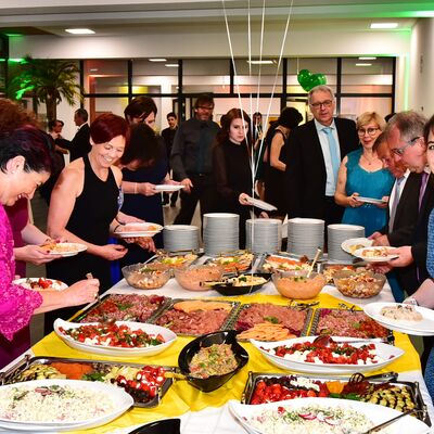 Foto des vielfältigen Buffets und lächelnden Menschen, die sich etwas zu essen nehmen.
