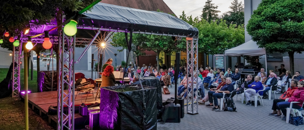 Fotografie des Auftritts der Kabarettistin Lizzy Aumeier. Der Hof vor dem Rathaus ist mit Besuchern gefüllt. Die Bühne ist lila beleuchtet.
