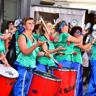 Bild vergrößern: Foto einer Trommelgruppe, die alle grüne Oberteile, blaue Hosen und rote Trommeln tragen.