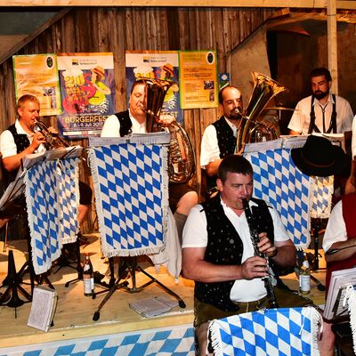 Bild vergrößern: Foto von Personen in Tracht, die auf Blasinstrumenten musizieren. An den Notenständern sind bayrische Flaggen angebracht.