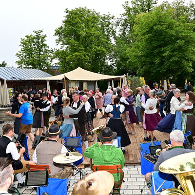 Bild vergrößern: Im Stadtpark ist ein Tanzboden aufgebaut, darauf tanzen viele Paare in bayerischer Tracht. Im Vordergrund ist eine Blaskapelle zu sehen.