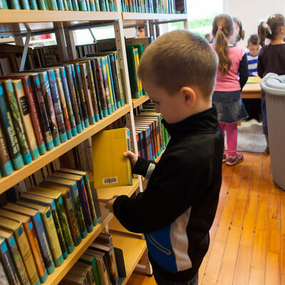 Bild vergrößern: Kind steht am Bücherregal