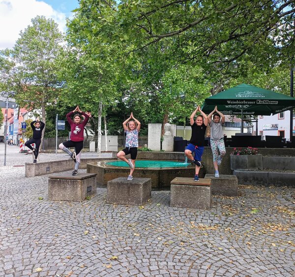 Bild vergrößern: 5 Kinder stehen auf den Betonblöcken am Kolpingplatz in der Haltung des Baumes.