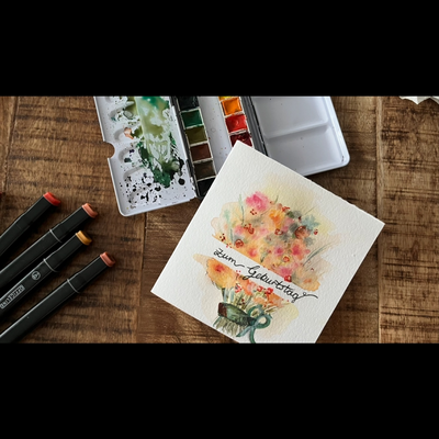 Eine Karte auf die ein Blumenstrau&szlig; mit Aquarell gemalt ist daneben in Aquarellmalkasten und bunte Marker.