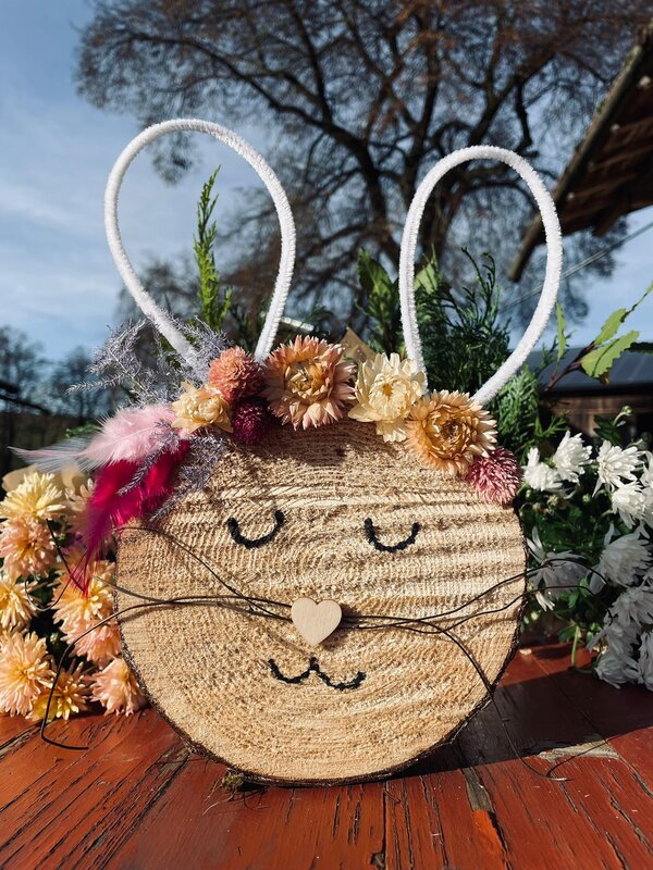 Bild vergr&ouml;&szlig;ern: Auf eine Holzscheibe ist ein Hasengesicht gemalt. Er hat Ohren aus wei&szlig;en Pfeiffenputzern und einen Blumenkranz