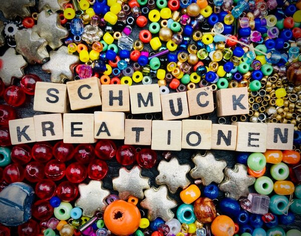 Bild vergr&ouml;&szlig;ern: Viele bunte Perlen. Aus Holzbuchstaben ist das Wort "Schmuckkreationen" gelegt.