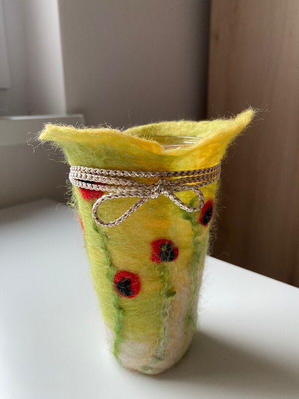 Bild vergr&ouml;&szlig;ern: Eine gelbe Filzh&uuml;lle mit roten Blumen, die um ein Windlicht gewickelt ist.