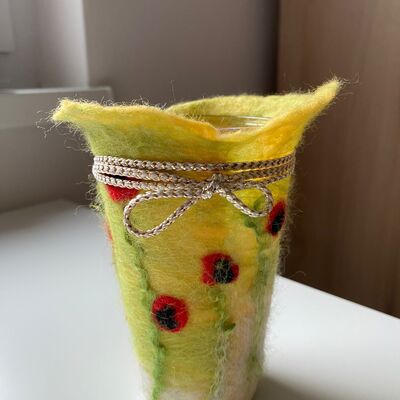Eine gelbe Filzh&uuml;lle mit roten Blumen, die um ein Windlicht gewickelt ist.