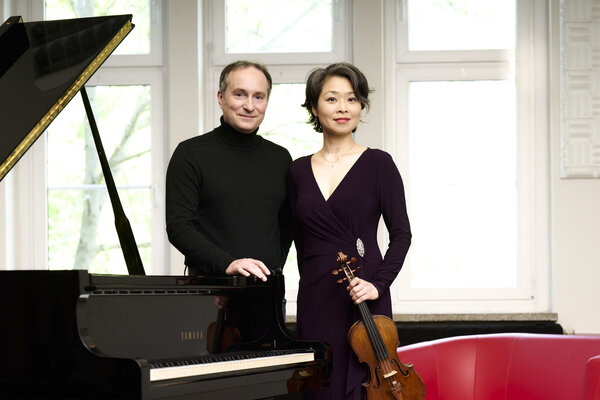Bild vergr&ouml;&szlig;ern: Der Pianist Christian Seibert neben einem offenen Fl&uuml;gel, neben ihm die Violinistin Jung Won Seibert-Oh mit ihrem Instrument in der Hand. Beide sind schwarz gekleidet.