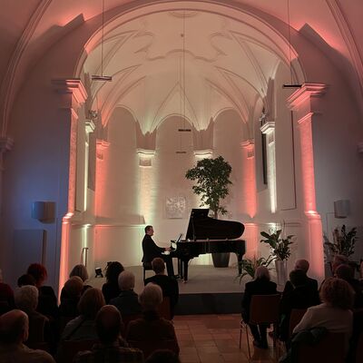 Bild vergr&ouml;&szlig;ern: Henri Sigfridsson spielt auf dem Klavier Werke von Franz Schubert und Wolfgang Amadeus Mozart mit Bearbeitungen von Franz Liszts in der rot-gelb beleuchteten Spitalkirche.