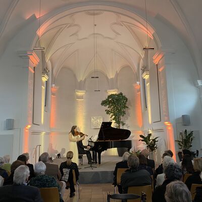 Bild vergr&ouml;&szlig;ern: Jung Won Seibert-Oh spielt auf der Violine und Christian Seibert auf dem Klavier und das Publikum h&ouml;rt dem Konzert gespannt zu.