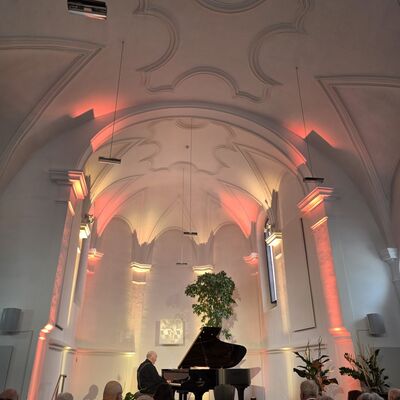 Bild vergr&ouml;&szlig;ern: Kurt Seibert spielt eine Klaviermatin&eacute;e in der orange-gelb beleuchteten Spitalkirche.