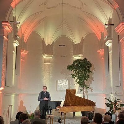 Bild vergr&ouml;&szlig;ern: Oliver Drechsel bedankt sich beim Publikum nach seinem Konzert in der Spitalkirche, die orange-gelb beleuchtet ist.