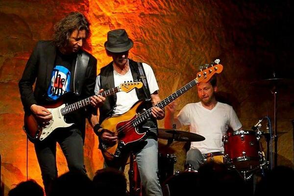 Bild vergrößern: Foto von der Van Straaten Band, die auf der Bühne im Kulturkeller performt. Der Hintergrund ist orange beleuchtet.