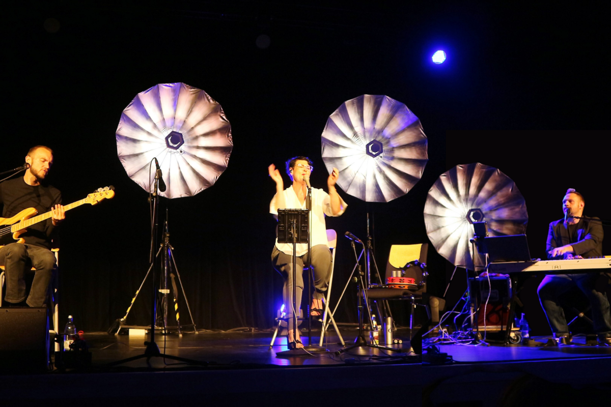 Foto der Band Soulfood unplugged, die auf einer dunklen Bhne performt. Im Hintergrund sind helle Schirmlampen zu sehen.
