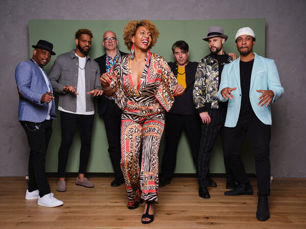 Bild vergr&ouml;&szlig;ern: Die S&auml;ngerin Yeni Toro tanzt in einem bunten Anzug im Vordergrund. Hinter ihr stehen die sechs Mitglieder ihrer Band.