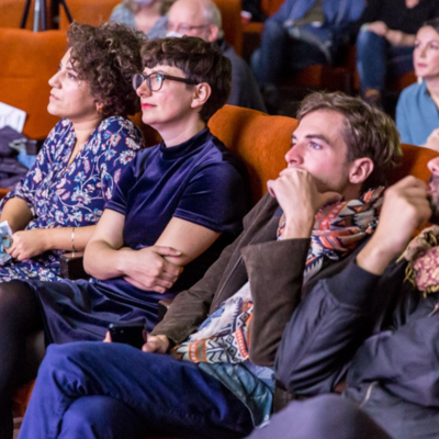 Bild vergr&ouml;&szlig;ern: Foto von mehreren Personen, die in roten Kino-Sesseln sitzen.