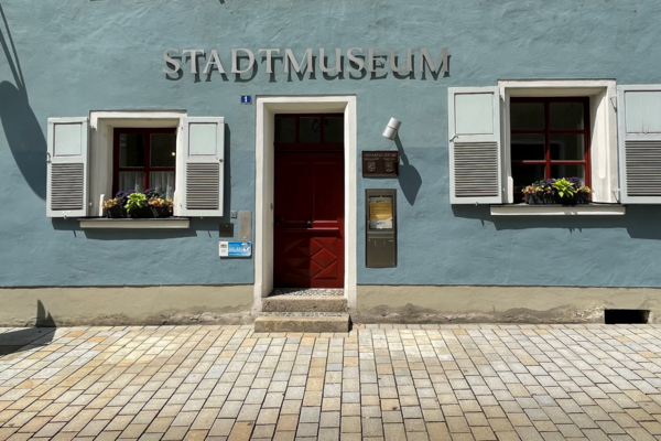 Foto des Eingangs des Stadtmuseums. Es ist eine rote Tür, eine blaue Fassade und ein silberner Schriftzug "Stadtmuseum" zu sehen.