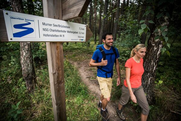 Eine Frau und ein Mann in Wanderkleidung und mit Rucksack marschieren auf einem Wanderweg im Wald.