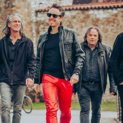 Die f&uuml;nf Musiker der Band Mad Company im Gehen fotografiert. Alle sind in Schwarz und Rot gekleidet.