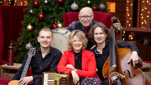 Die vier Mitglieder der Band Orchestra Mondo posieren mit ihren Instrumenten, einem Schlagzeug, einer Gitarre, einem Akkordeon und einem Kontrabass vor einem geschm&uuml;ckten Weihnachtsbaum. 