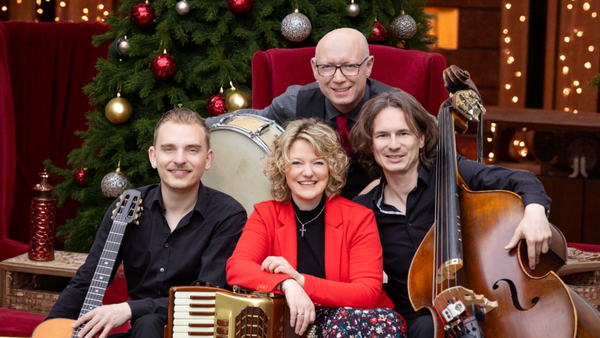 Die vier Mitglieder der Band Orchestra Mondo posieren mit ihren Instrumenten, einem Schlagzeug, einer Gitarre, einem Akkordeon und einem Kontrabass vor einem geschm&uuml;ckten Weihnachtsbaum. 