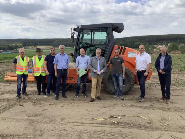Bild vergrößern: Neun Männer vor einem Bagger auf einer Baustelle.