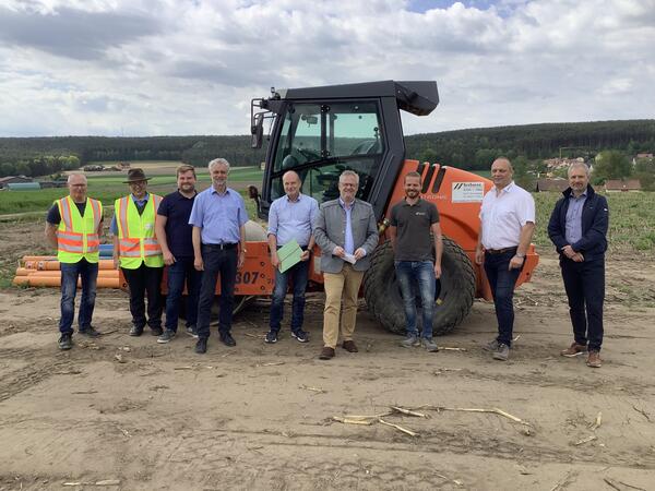 Bild vergrößern: Neun Mnner vor einem Bagger auf einer Baustelle.