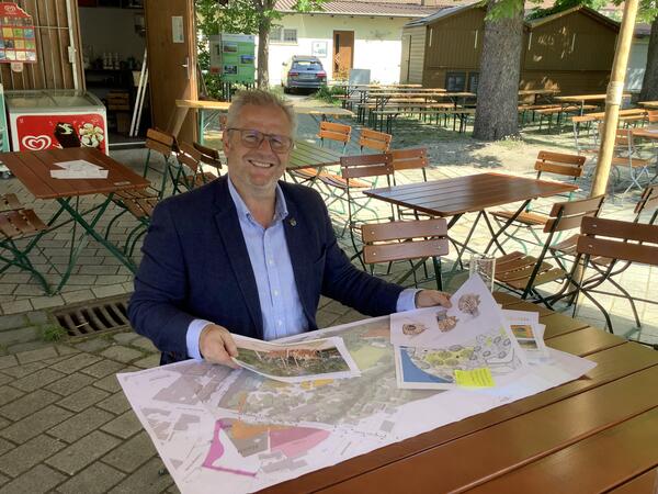 Ein Mann sitzt an einem Tisch in einem Biergarten und schaut sich Plne an.