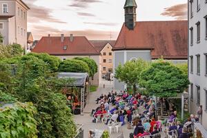 Bild vergrößern: Luftaufnahme des Spitalgartens. Die zahlreichen Besucher:innen sitzen  in weißen Stühlen vor der Open-Air-Bühne, auf der gerade eine Band performt.