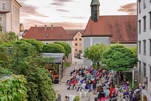 Bild vergrößern: Luftaufnahme des Spitalgartens. Die zahlreichen Besucher:innen sitzen  in weien Sthlen vor der Open-Air-Bhne, auf der gerade eine Band performt.