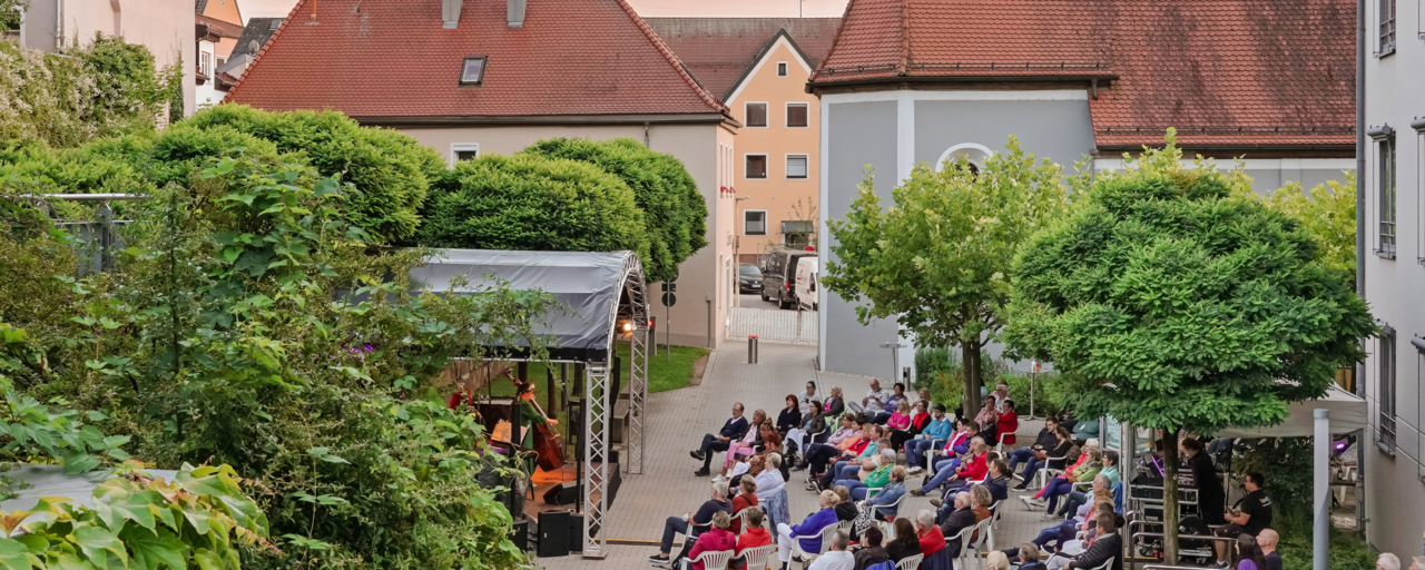 Luftaufnahme des Spitalgartens. Die zahlreichen Besucher:innen sitzen  in weißen Stühlen vor der Open-Air-Bühne, auf der gerade eine Band performt. 