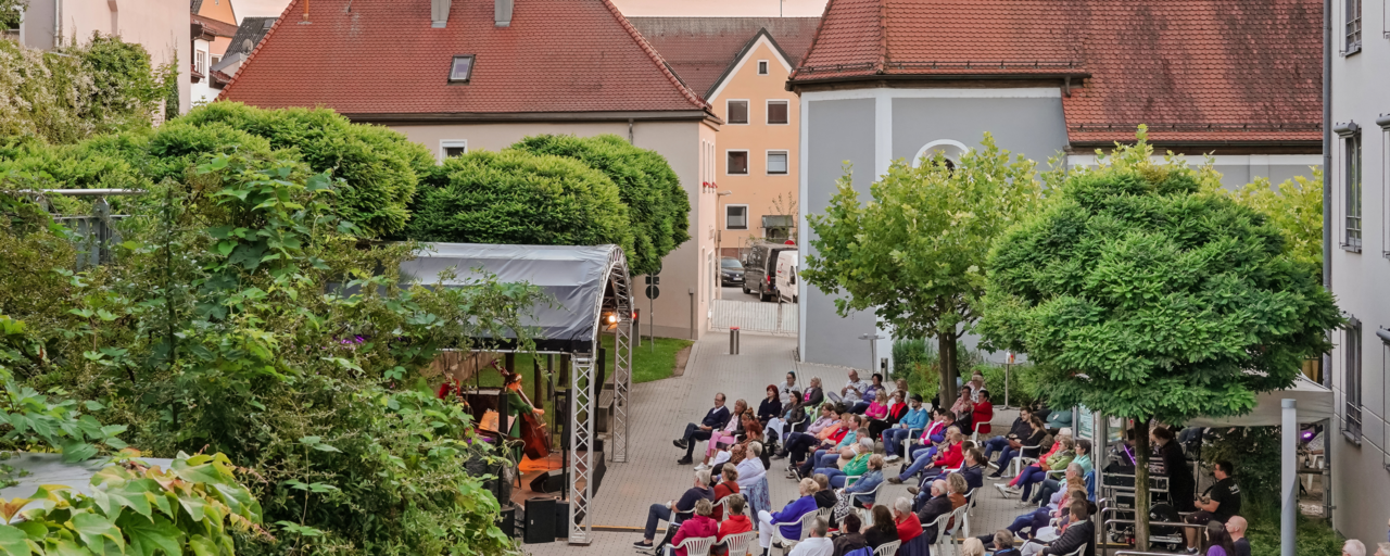 Luftaufnahme des Spitalgartens. Die zahlreichen Besucher:innen sitzen  in weien Sthlen vor der Open-Air-Bhne, auf der gerade eine Band performt. 