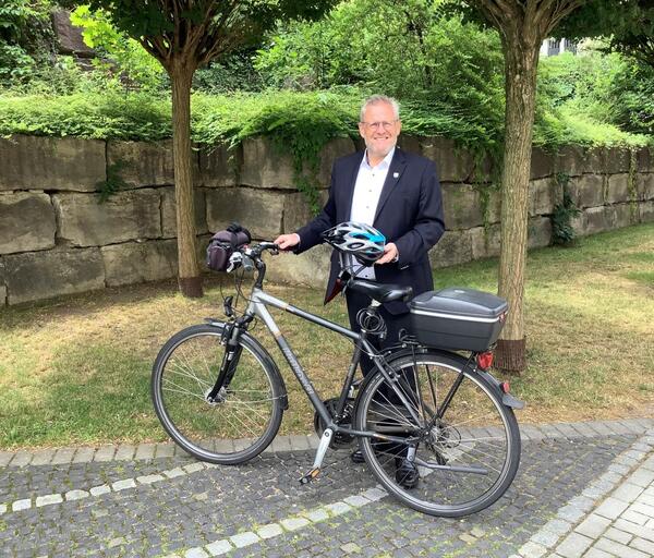 Bild vergrößern: Ein Mann steht neben einem Fahrrad und hat einen Fahrradhelm in der Hand.